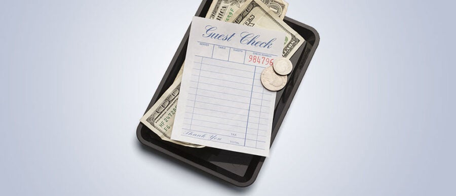 A restaurant guest check with a number printed on it, placed on a black tray, accompanied by cash and coins.