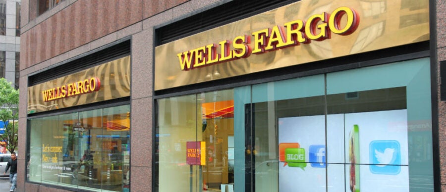 The image shows the exterior of a Wells Fargo bank branch with its logo prominently displayed above the entrance.