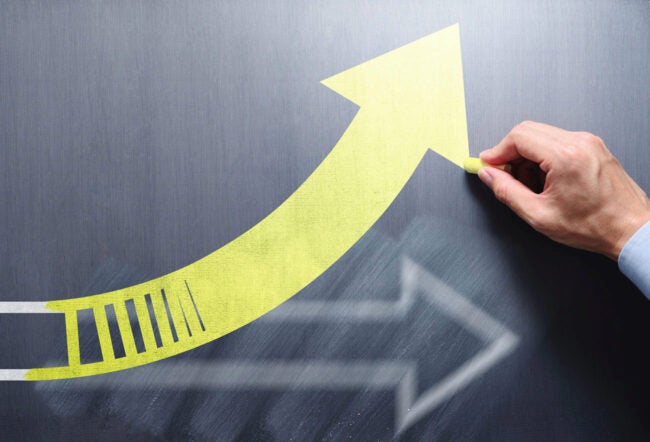 A person's hand drawing a new arrow over an erased arrow on the chalkboard